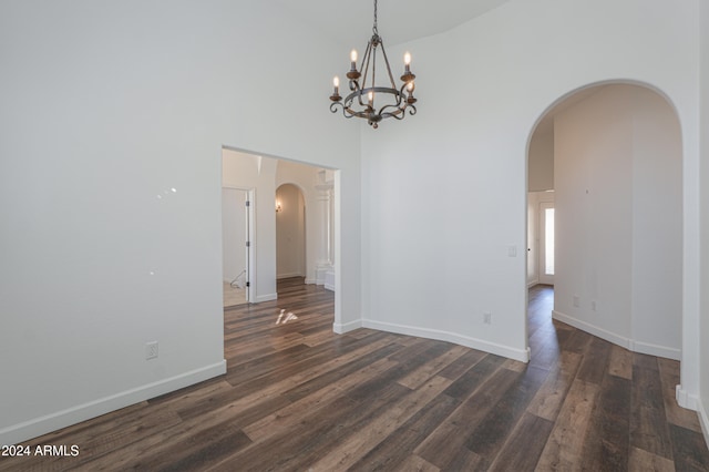 empty room featuring a notable chandelier, dark hardwood / wood-style floors, and high vaulted ceiling