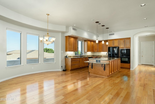 kitchen with a kitchen bar, decorative light fixtures, a kitchen island with sink, light hardwood / wood-style flooring, and black appliances