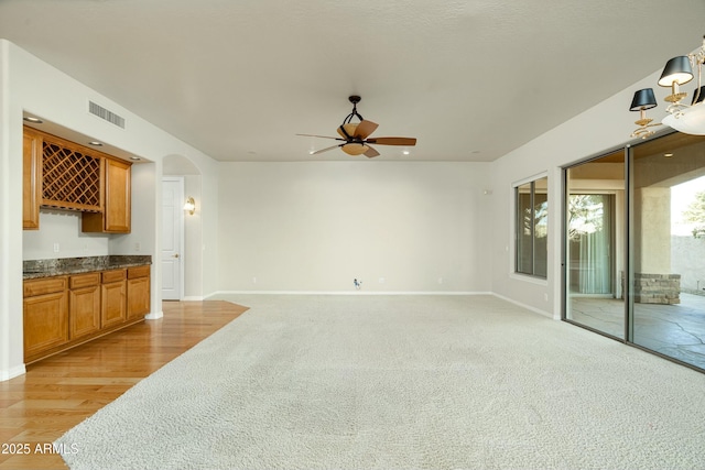 unfurnished living room featuring ceiling fan, bar area, and light hardwood / wood-style floors