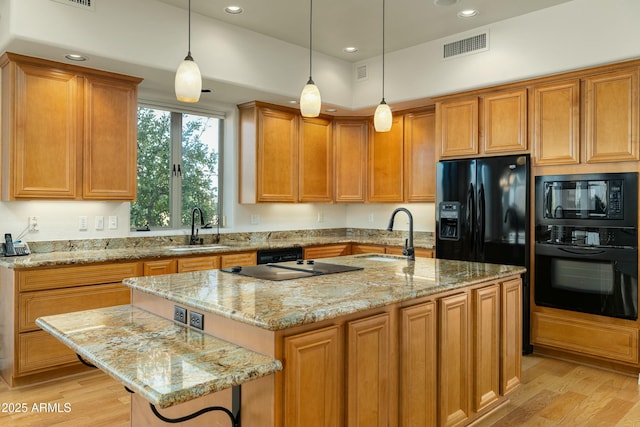 kitchen with decorative light fixtures, a center island with sink, black appliances, sink, and light stone countertops