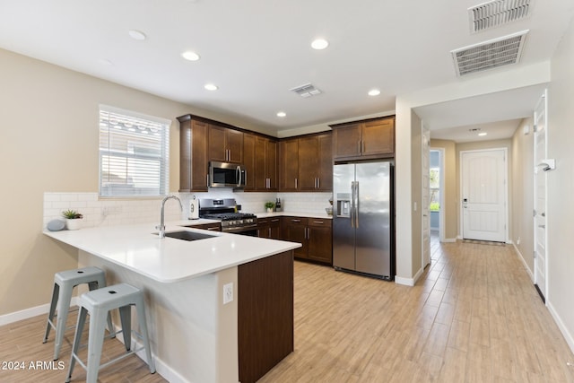 kitchen with kitchen peninsula, decorative backsplash, appliances with stainless steel finishes, light wood-type flooring, and sink