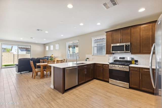 kitchen featuring tasteful backsplash, sink, kitchen peninsula, stainless steel appliances, and light hardwood / wood-style flooring