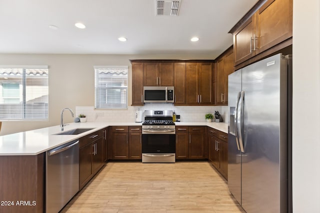 kitchen featuring sink, backsplash, kitchen peninsula, light hardwood / wood-style floors, and stainless steel appliances