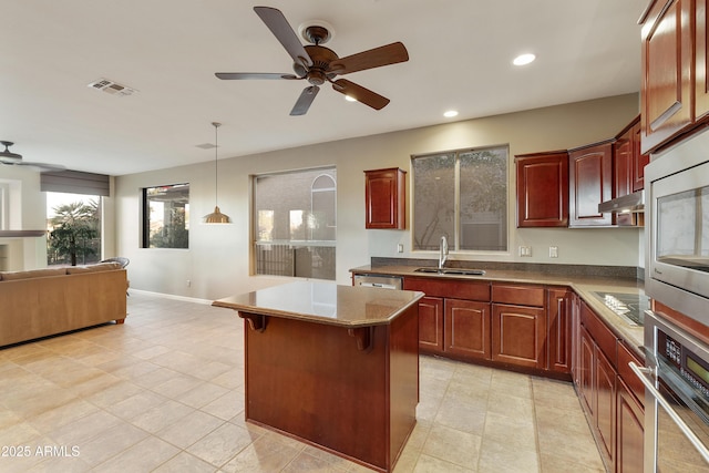 kitchen with ceiling fan, sink, stainless steel appliances, decorative light fixtures, and a kitchen bar