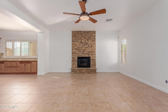 unfurnished living room featuring ceiling fan, light tile patterned floors, a fireplace, and a wealth of natural light