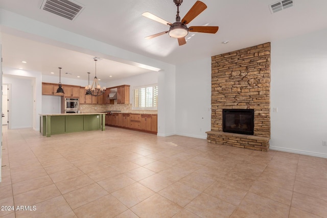 unfurnished living room with ceiling fan with notable chandelier, a stone fireplace, and light tile patterned floors