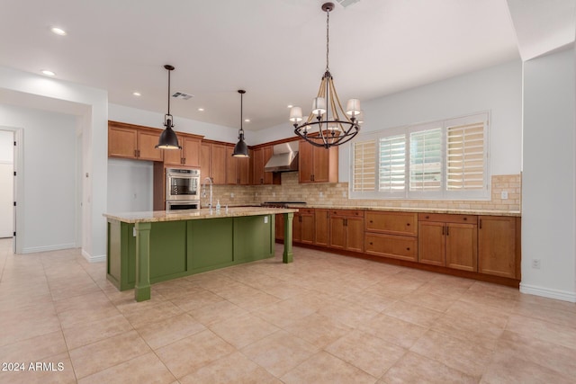 kitchen with decorative light fixtures, a center island with sink, wall chimney exhaust hood, and a notable chandelier