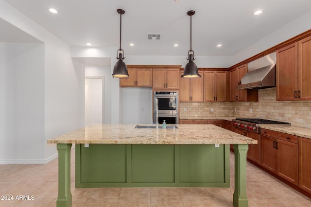 kitchen with light stone countertops, an island with sink, extractor fan, decorative light fixtures, and appliances with stainless steel finishes