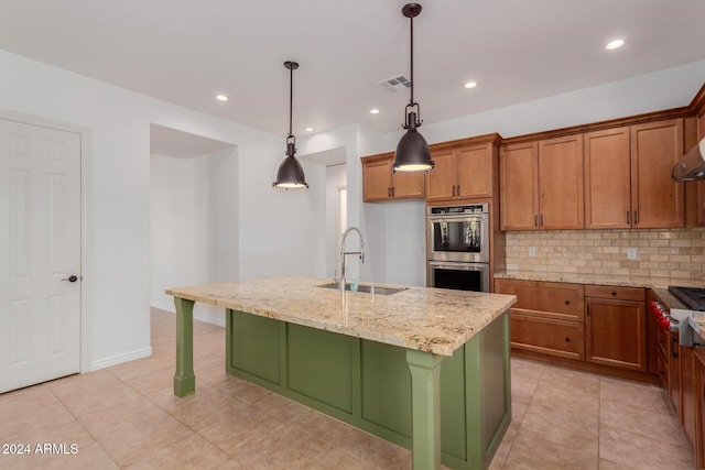 kitchen with a center island with sink, sink, hanging light fixtures, light stone counters, and stainless steel double oven