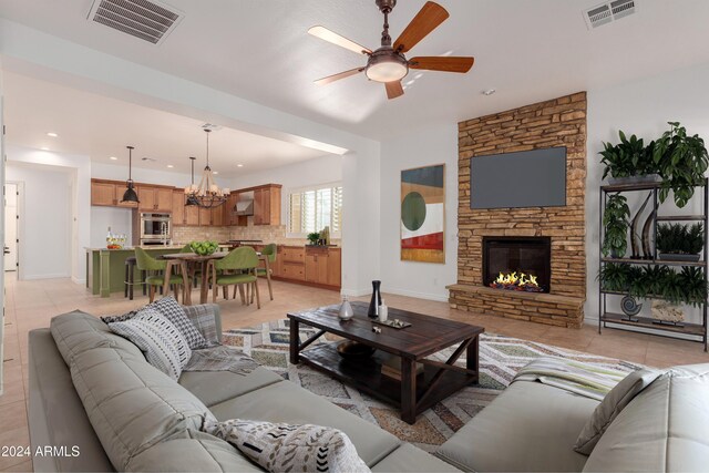 tiled living room featuring ceiling fan with notable chandelier and a stone fireplace