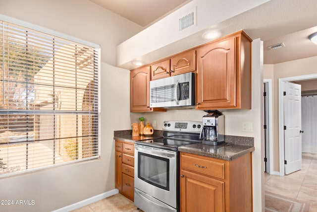 kitchen featuring light tile patterned flooring, appliances with stainless steel finishes, and dark stone counters