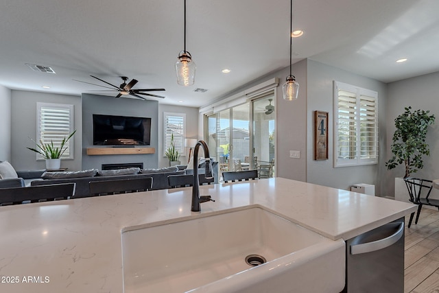 kitchen featuring pendant lighting, sink, light stone counters, and ceiling fan