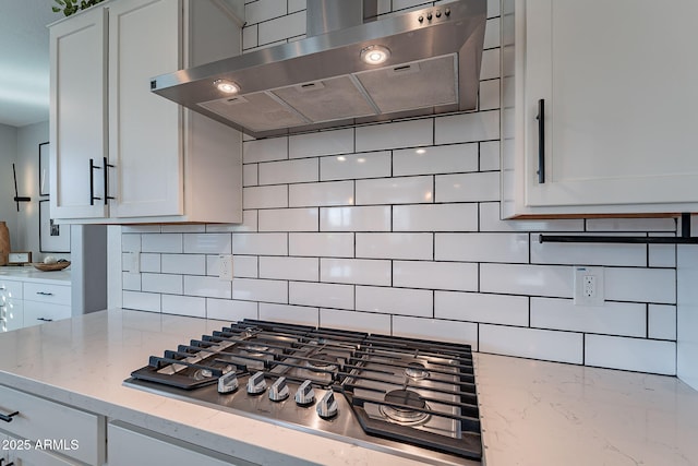 kitchen featuring light stone countertops, range hood, stainless steel gas cooktop, and white cabinets