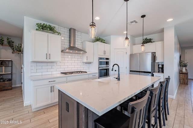 kitchen featuring white cabinetry, appliances with stainless steel finishes, wall chimney exhaust hood, and a kitchen island with sink