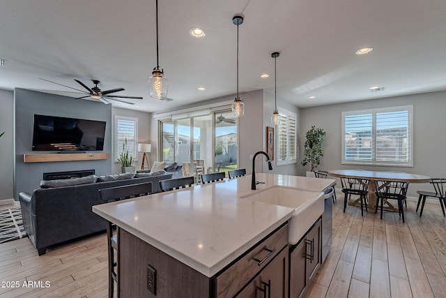 kitchen featuring an island with sink, light wood-type flooring, light stone counters, and decorative light fixtures