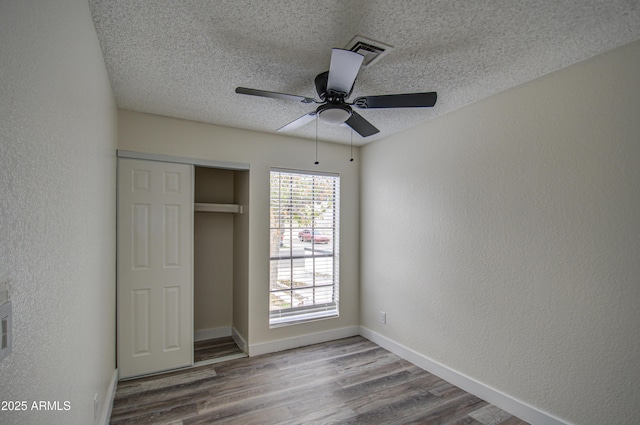 unfurnished bedroom with ceiling fan, a closet, hardwood / wood-style floors, and a textured ceiling