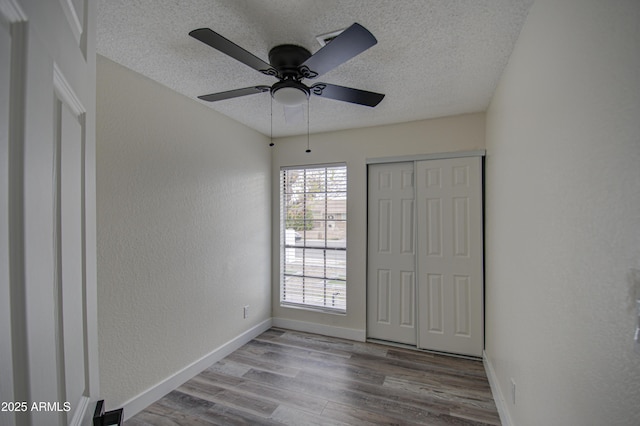 unfurnished bedroom with ceiling fan, a closet, a textured ceiling, and hardwood / wood-style flooring