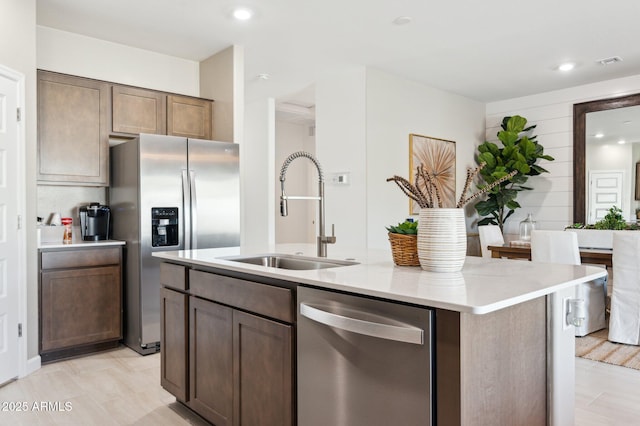 kitchen with appliances with stainless steel finishes, sink, a kitchen island with sink, and dark brown cabinetry