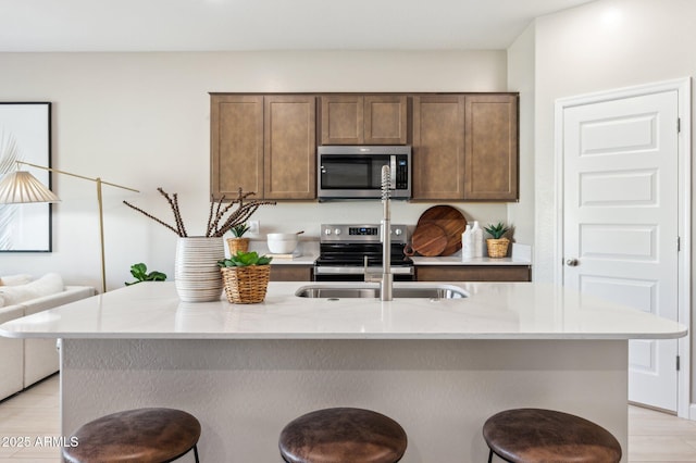 kitchen with light stone counters, appliances with stainless steel finishes, sink, and an island with sink