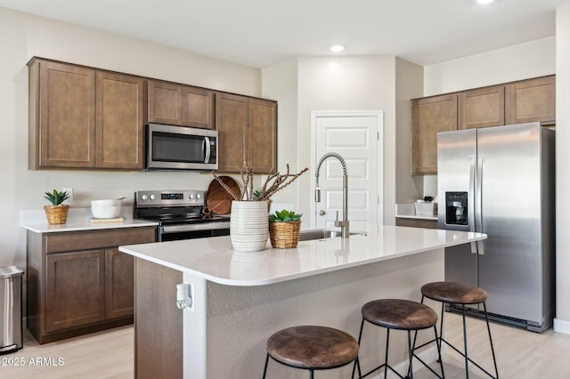 kitchen featuring a kitchen island with sink, sink, a breakfast bar, and appliances with stainless steel finishes