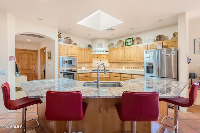 kitchen with sink, a kitchen bar, a large island, stainless steel appliances, and light stone countertops