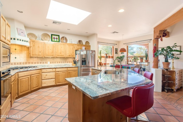 kitchen with a breakfast bar, an island with sink, sink, stainless steel appliances, and light brown cabinets