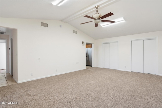 unfurnished bedroom featuring stainless steel refrigerator with ice dispenser, two closets, lofted ceiling with beams, ceiling fan, and light colored carpet