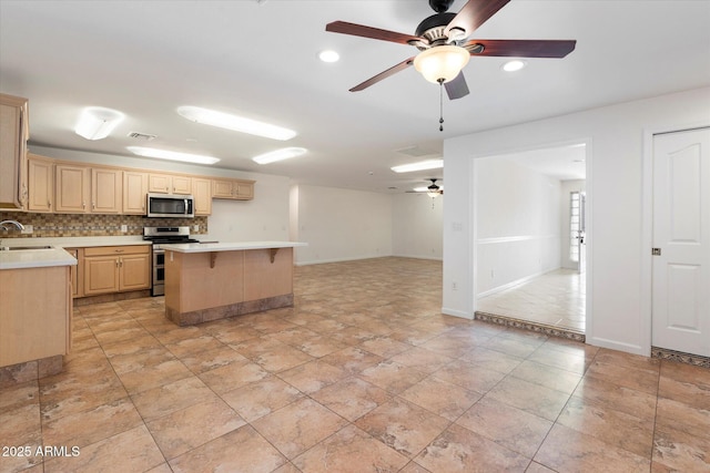 kitchen with appliances with stainless steel finishes, a kitchen island, light brown cabinetry, sink, and decorative backsplash