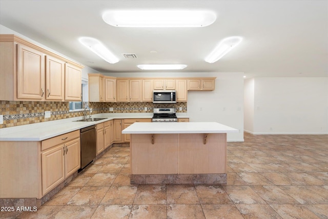 kitchen featuring light brown cabinets, sink, a kitchen bar, a kitchen island, and stainless steel appliances