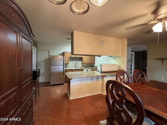 kitchen featuring a sink, ceiling fan, a peninsula, dark tile patterned floors, and freestanding refrigerator