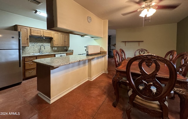 kitchen featuring a sink, a ceiling fan, a peninsula, dark tile patterned floors, and freestanding refrigerator