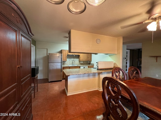 kitchen with stainless steel refrigerator, ceiling fan, sink, kitchen peninsula, and dark tile patterned flooring