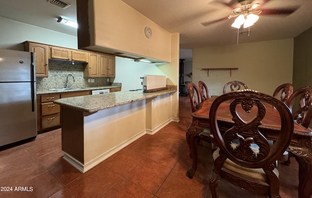 kitchen with light stone countertops, tasteful backsplash, sink, dark tile patterned flooring, and stainless steel refrigerator