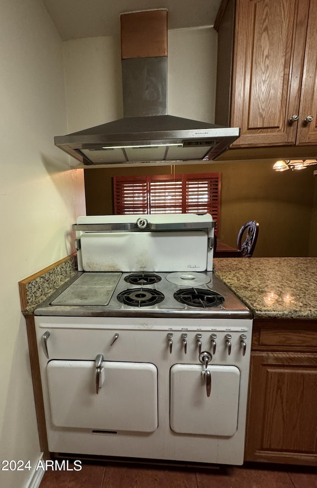 kitchen featuring dark tile patterned flooring, light stone countertops, white range oven, and wall chimney range hood