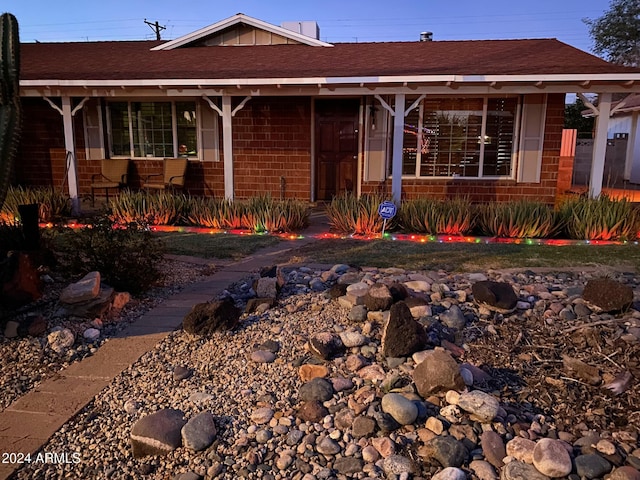 ranch-style house with roof with shingles, covered porch, and brick siding