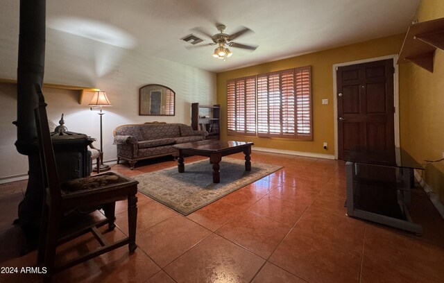 living area featuring a wood stove, visible vents, ceiling fan, baseboards, and tile patterned floors