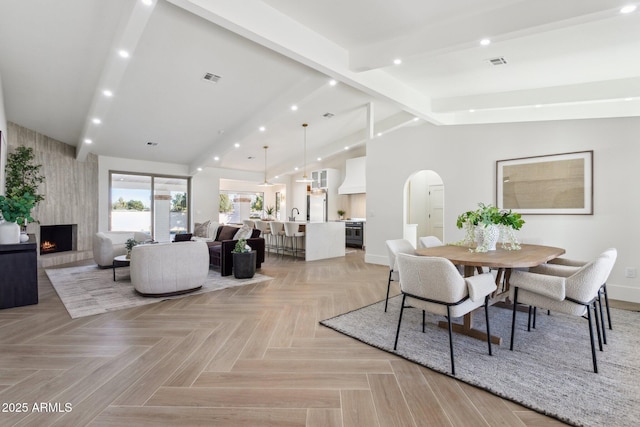 dining space with beamed ceiling, light parquet flooring, high vaulted ceiling, and a fireplace