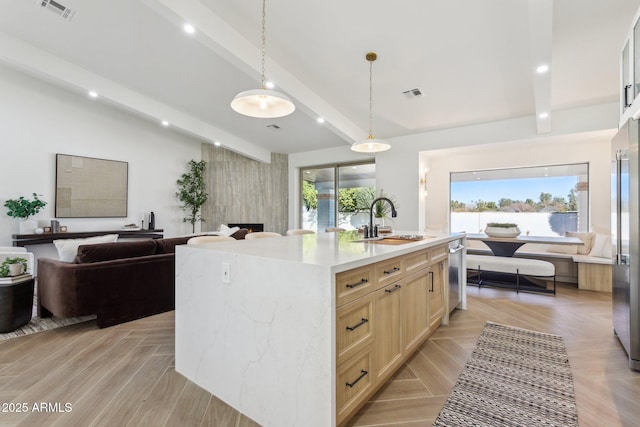 kitchen with pendant lighting, sink, a center island with sink, beamed ceiling, and light brown cabinets