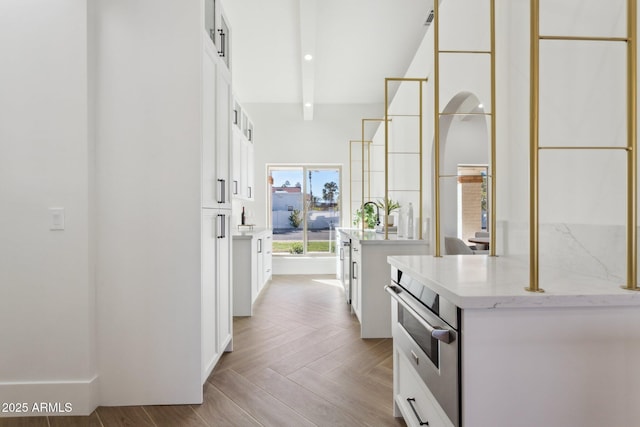 kitchen featuring white cabinetry, light stone countertops, light parquet flooring, and oven