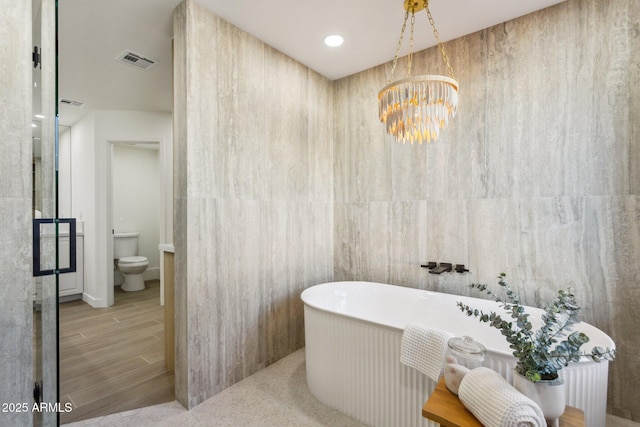 bathroom featuring tile walls, a chandelier, a bathtub, and toilet