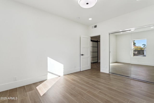 unfurnished bedroom with a barn door, a closet, and light wood-type flooring