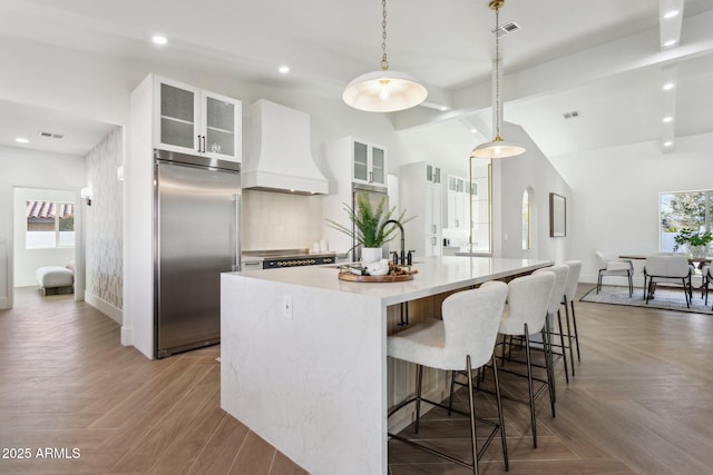 kitchen with premium range hood, built in refrigerator, pendant lighting, light parquet flooring, and a large island