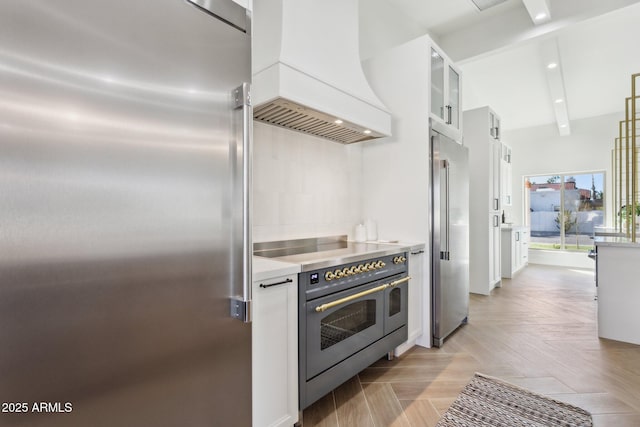 kitchen featuring high quality appliances, custom range hood, beamed ceiling, light parquet flooring, and white cabinets