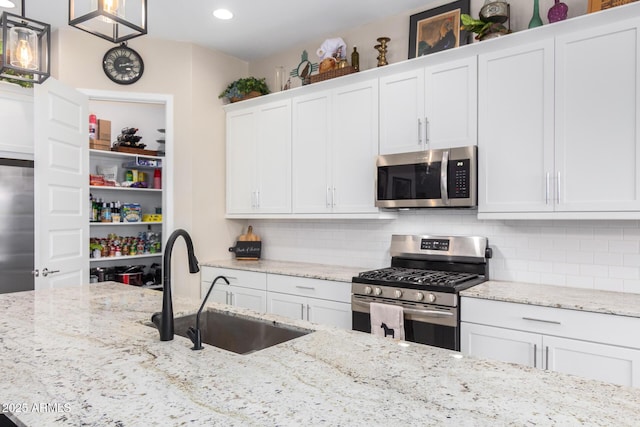 kitchen with sink, appliances with stainless steel finishes, white cabinetry, decorative backsplash, and decorative light fixtures