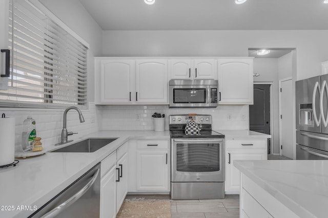 kitchen with decorative backsplash, white cabinetry, stainless steel appliances, and a sink