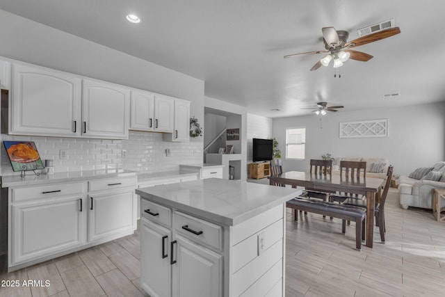 kitchen with visible vents, a ceiling fan, tasteful backsplash, open floor plan, and white cabinetry