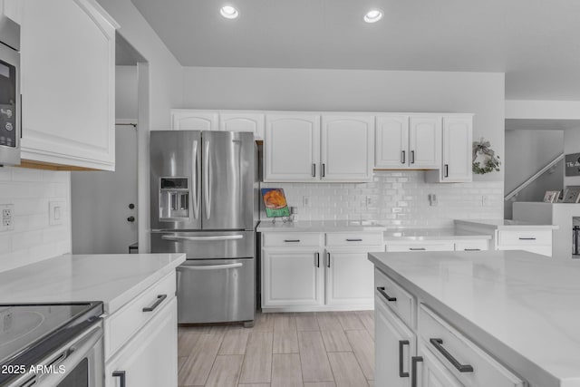 kitchen featuring tasteful backsplash, light stone countertops, recessed lighting, white cabinets, and stainless steel fridge