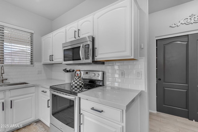 kitchen with a sink, backsplash, appliances with stainless steel finishes, white cabinets, and light countertops