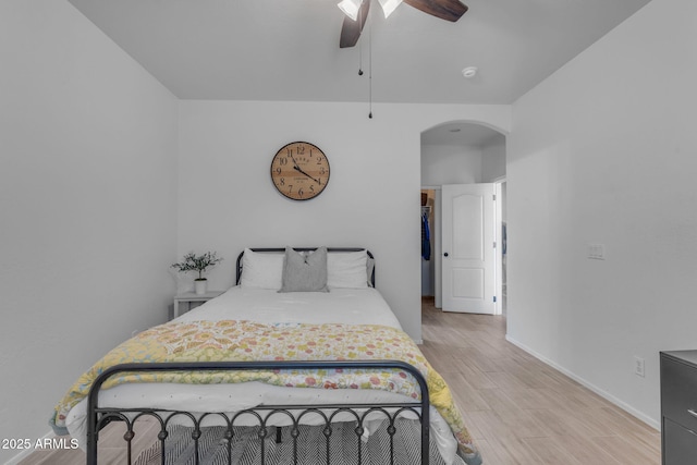 bedroom with light wood-type flooring, arched walkways, baseboards, and ceiling fan