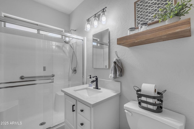 bathroom with vanity, toilet, a textured wall, and a stall shower